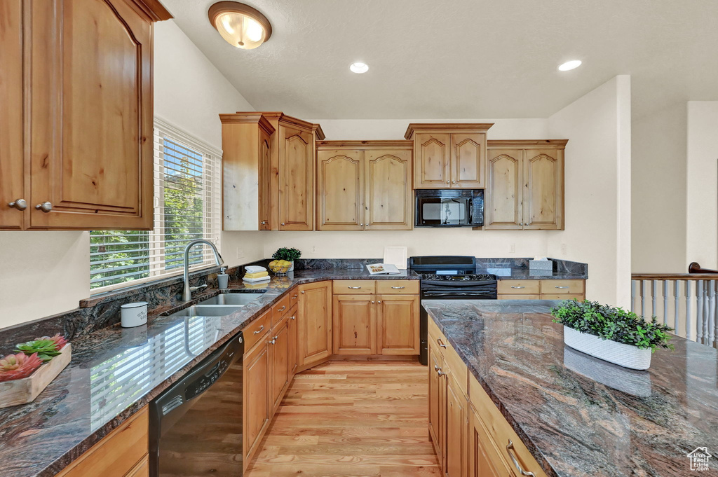 Kitchen with dark stone countertops, sink, black appliances, and light hardwood / wood-style floors