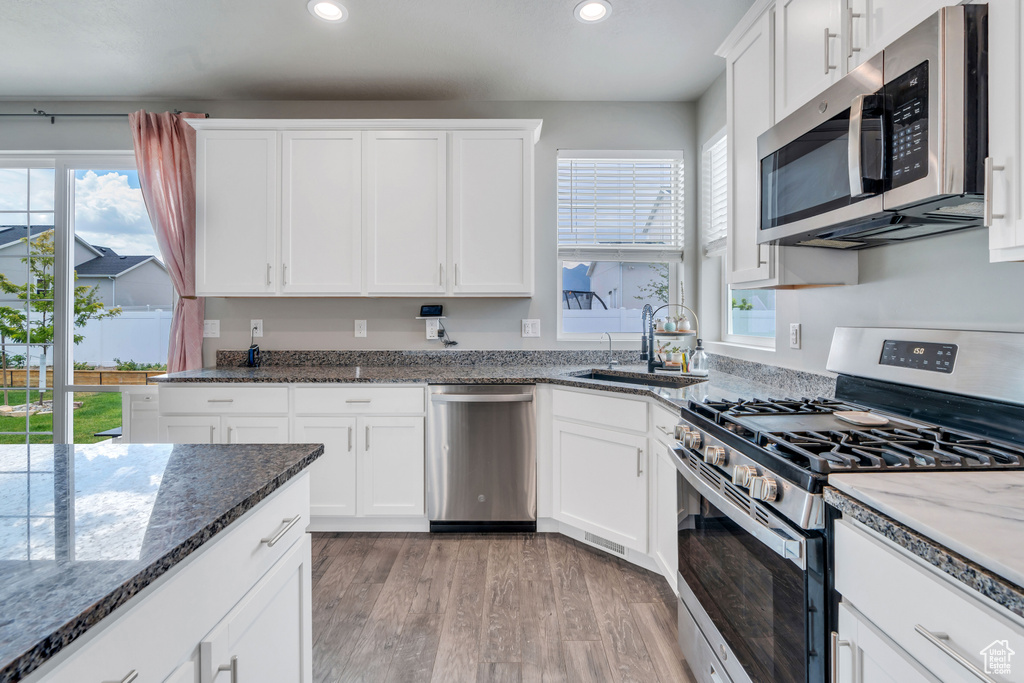 Kitchen with dark stone counters, stainless steel appliances, white cabinets, sink, and light wood-type flooring