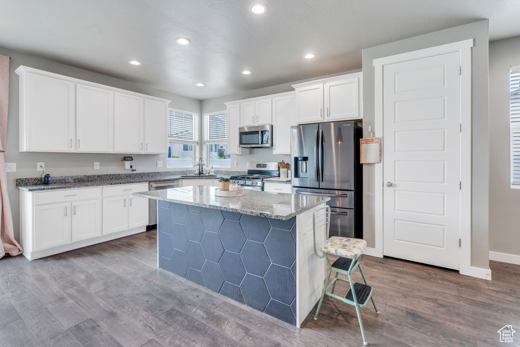 Kitchen with stone counters, stainless steel appliances, sink, a kitchen island, and hardwood / wood-style flooring