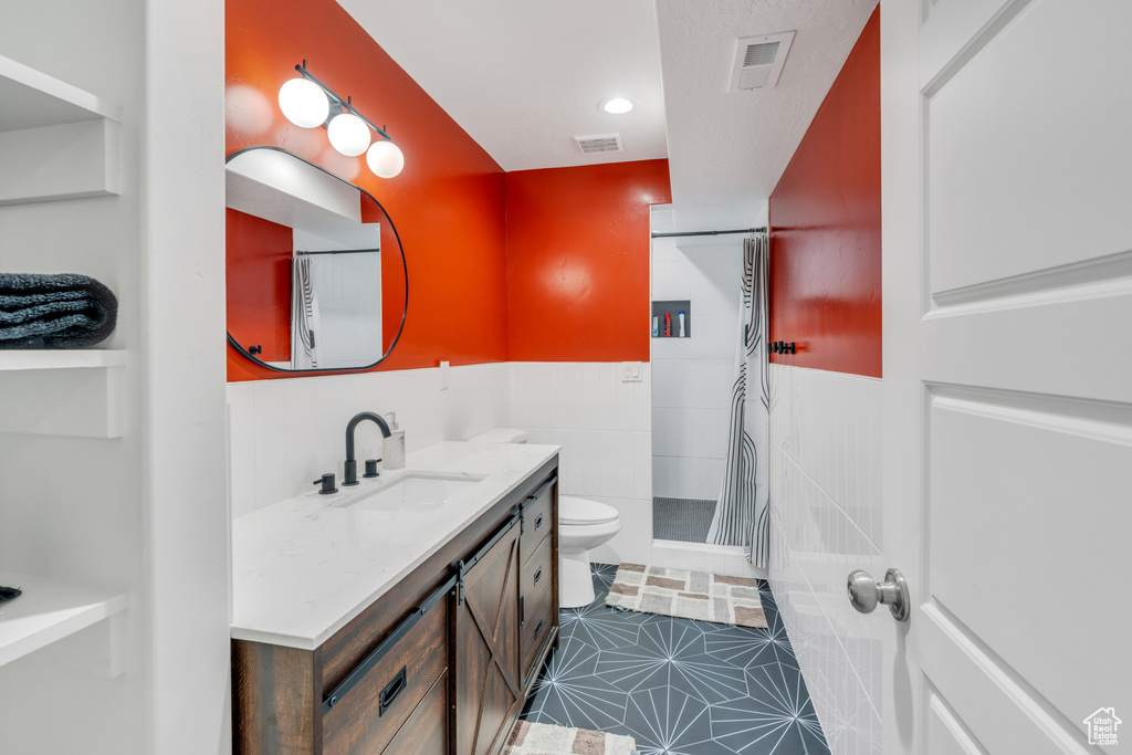 Bathroom with vanity, tile patterned floors, tile walls, a shower, and toilet