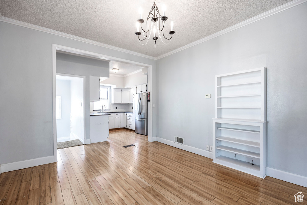 Unfurnished living room featuring a chandelier, a textured ceiling, light hardwood / wood-style flooring, and ornamental molding