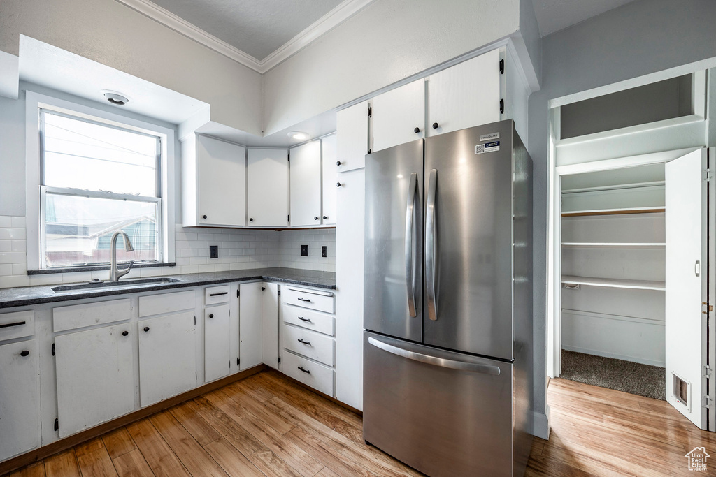 Kitchen with white cabinets, sink, stainless steel refrigerator, light hardwood / wood-style floors, and decorative backsplash