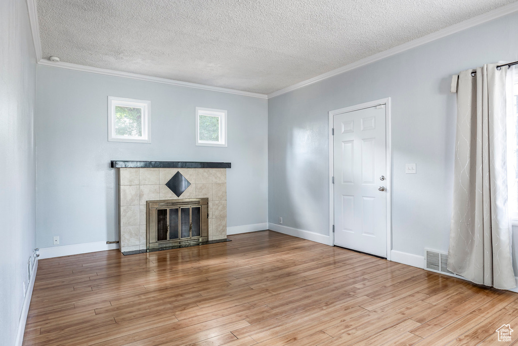 Unfurnished living room with a tiled fireplace, light wood-type flooring, crown molding, and a textured ceiling