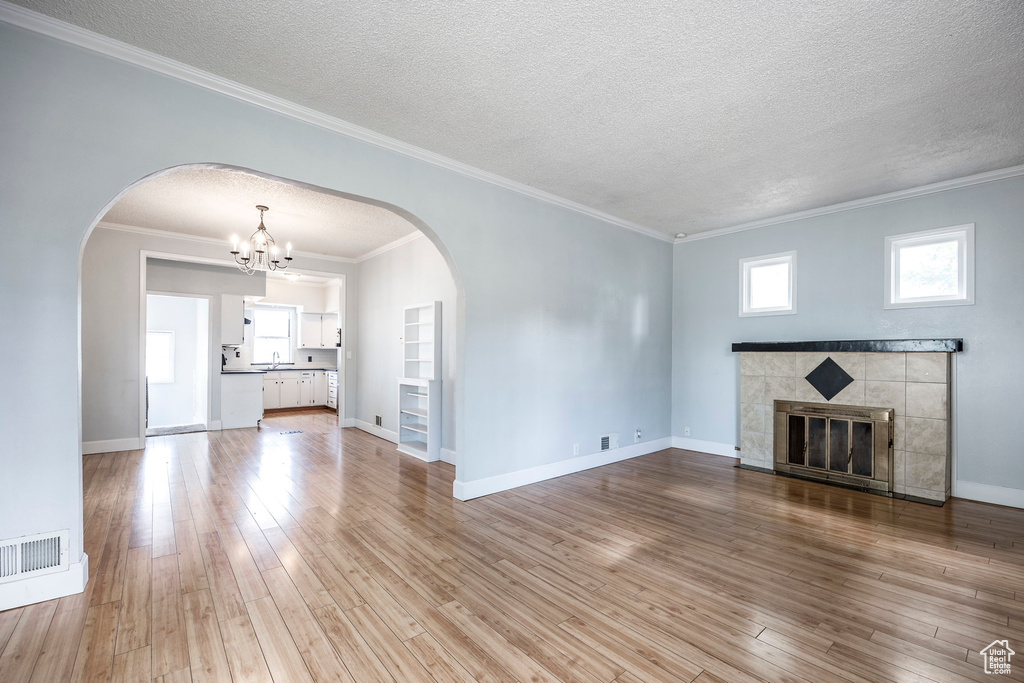 Unfurnished living room with a notable chandelier, crown molding, a textured ceiling, light hardwood / wood-style floors, and a tile fireplace