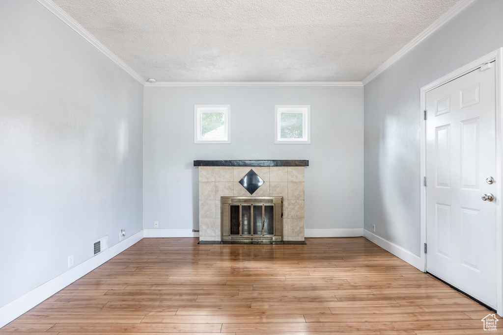 Unfurnished living room with light hardwood / wood-style floors, a tile fireplace, crown molding, and a textured ceiling