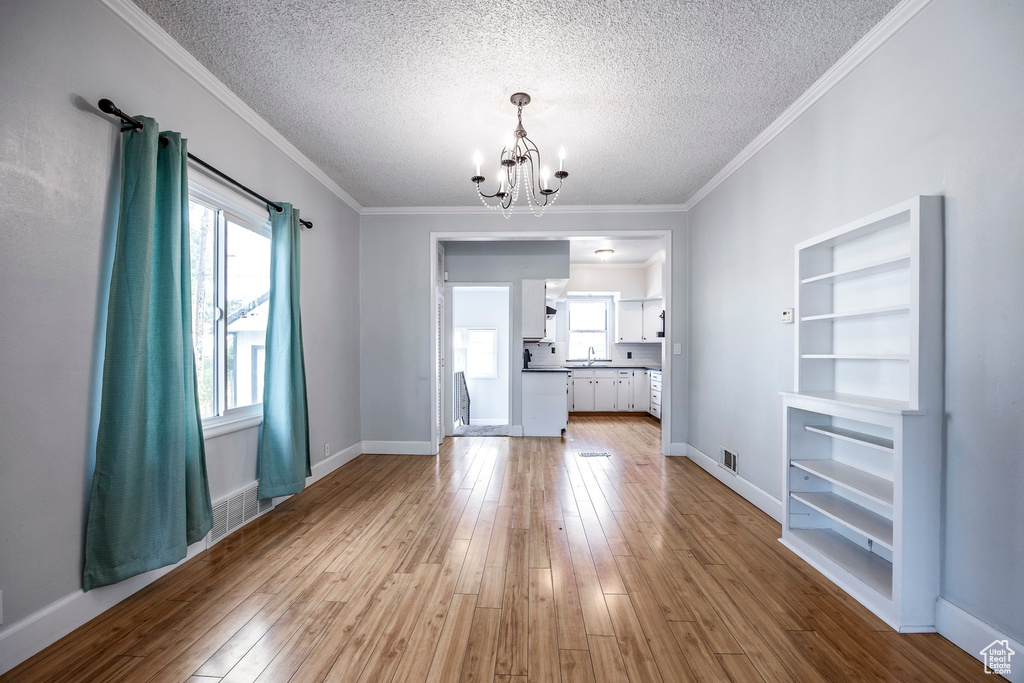 Unfurnished living room featuring wood-type flooring, a notable chandelier, ornamental molding, and a textured ceiling