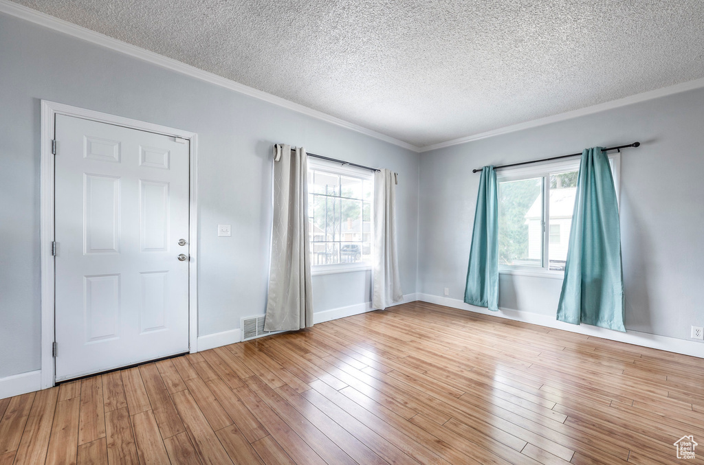 Spare room with light hardwood / wood-style floors, a textured ceiling, and ornamental molding