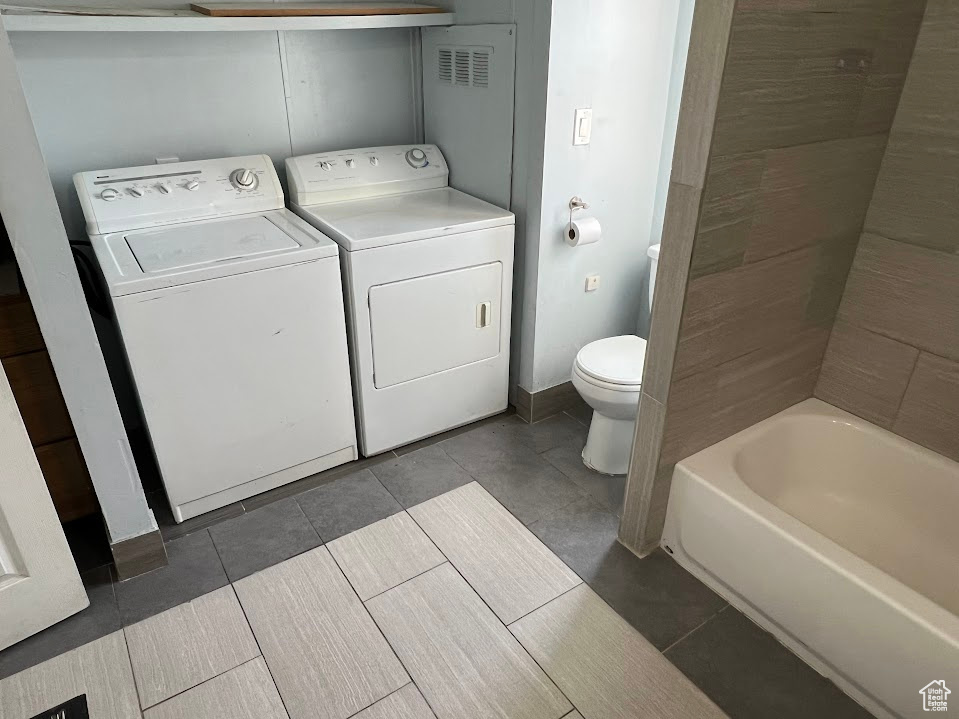 Interior space featuring a bath, toilet, washing machine and clothes dryer, and tile patterned floors