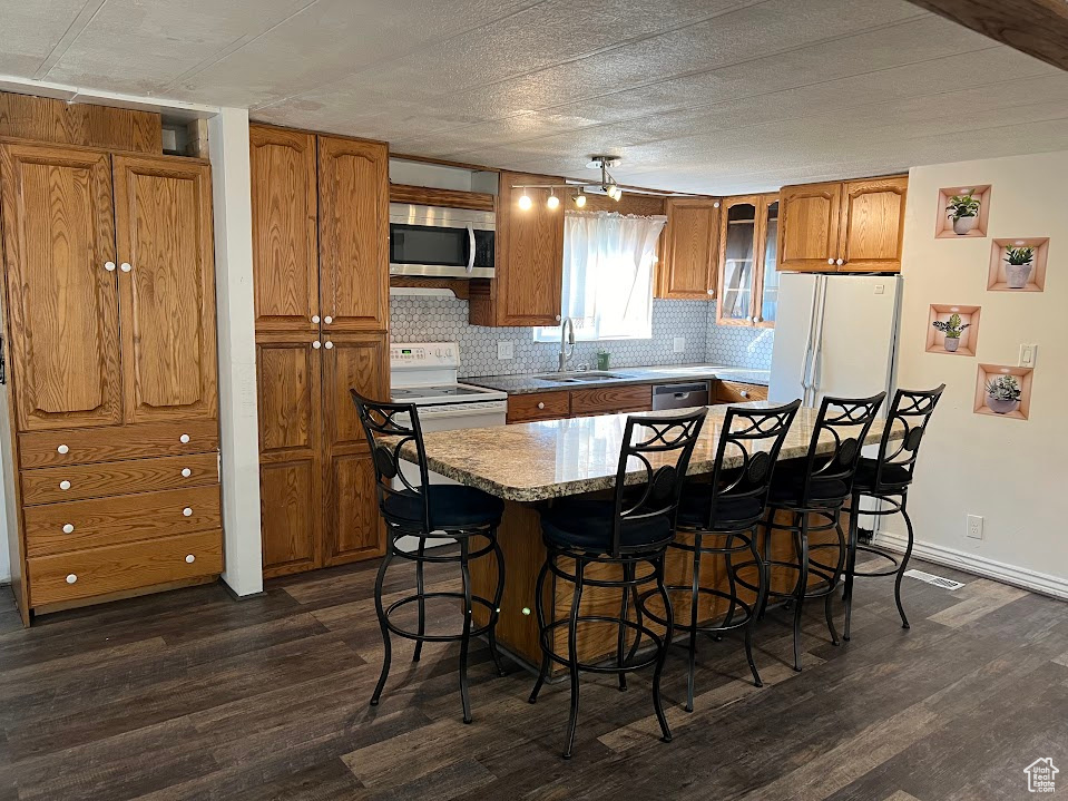 Kitchen featuring dark wood-type flooring, stainless steel appliances, sink, and a breakfast bar area