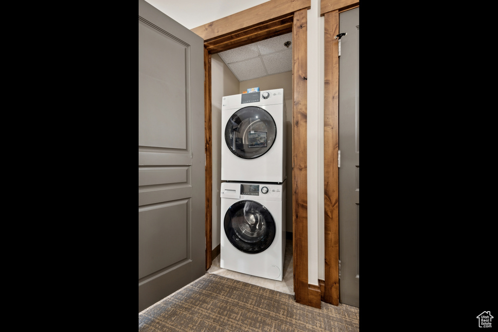 Washroom with stacked washer / drying machine and dark carpet