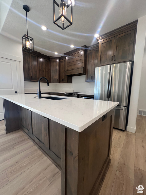 Kitchen featuring decorative light fixtures, premium range hood, light wood-type flooring, sink, and appliances with stainless steel finishes