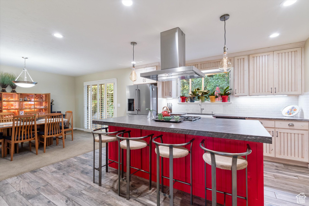 Kitchen with island exhaust hood, light carpet, a kitchen bar, high end refrigerator, and a kitchen island with sink