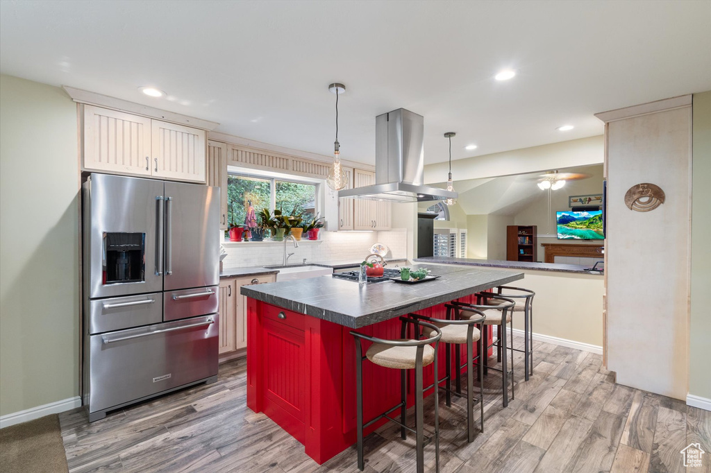 Kitchen featuring tasteful backsplash, a center island, light hardwood / wood-style floors, island range hood, and stainless steel refrigerator with ice dispenser