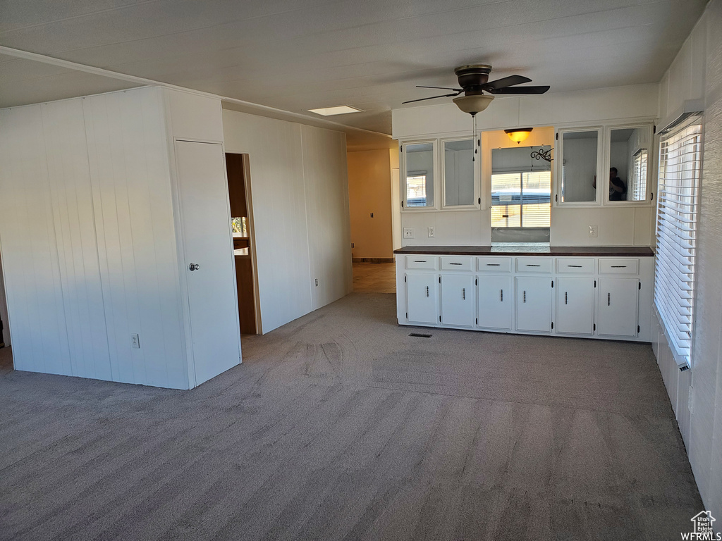 Kitchen with carpet floors, white cabinets, and ceiling fan