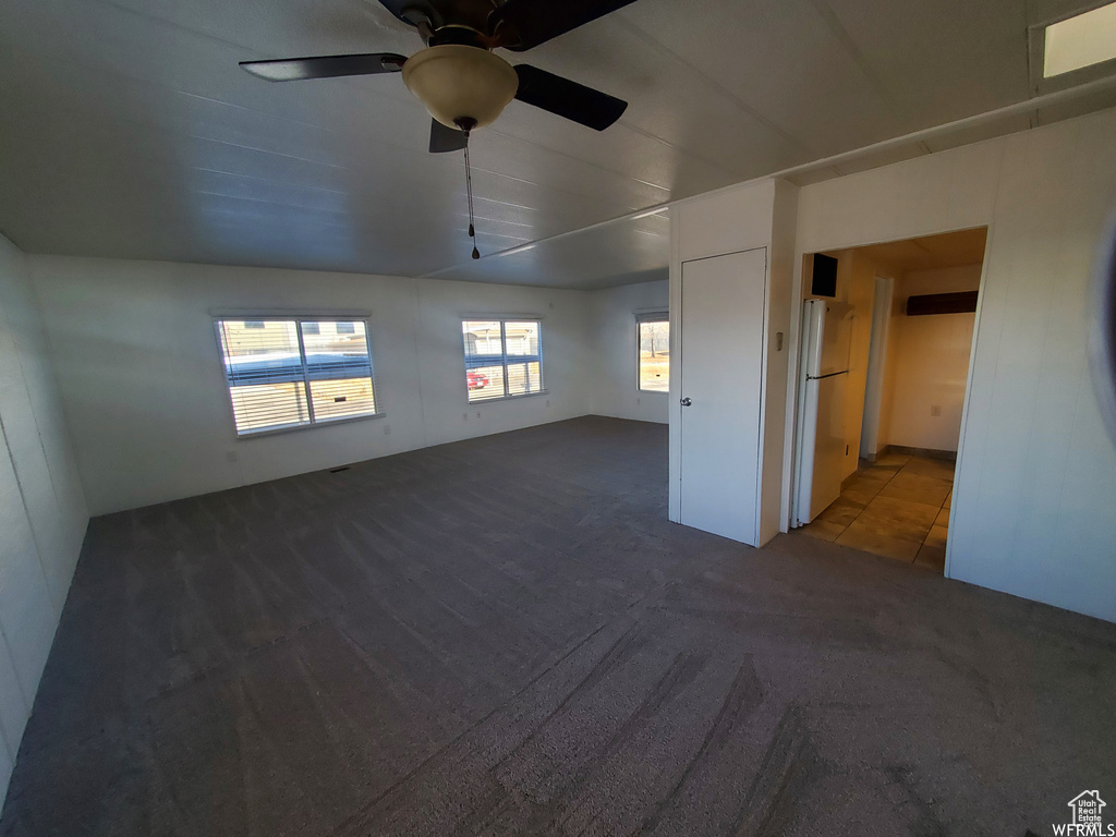 Unfurnished bedroom with carpet floors, white refrigerator, and ceiling fan