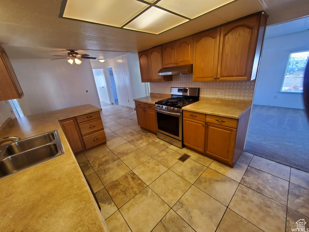 Kitchen featuring ceiling fan, decorative backsplash, stainless steel gas range oven, sink, and light tile patterned floors