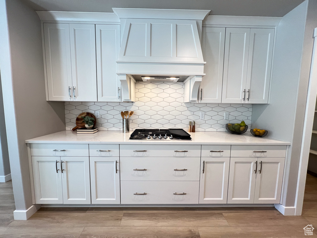 Kitchen featuring light hardwood / wood-style flooring, stainless steel gas stovetop, premium range hood, decorative backsplash, and white cabinets