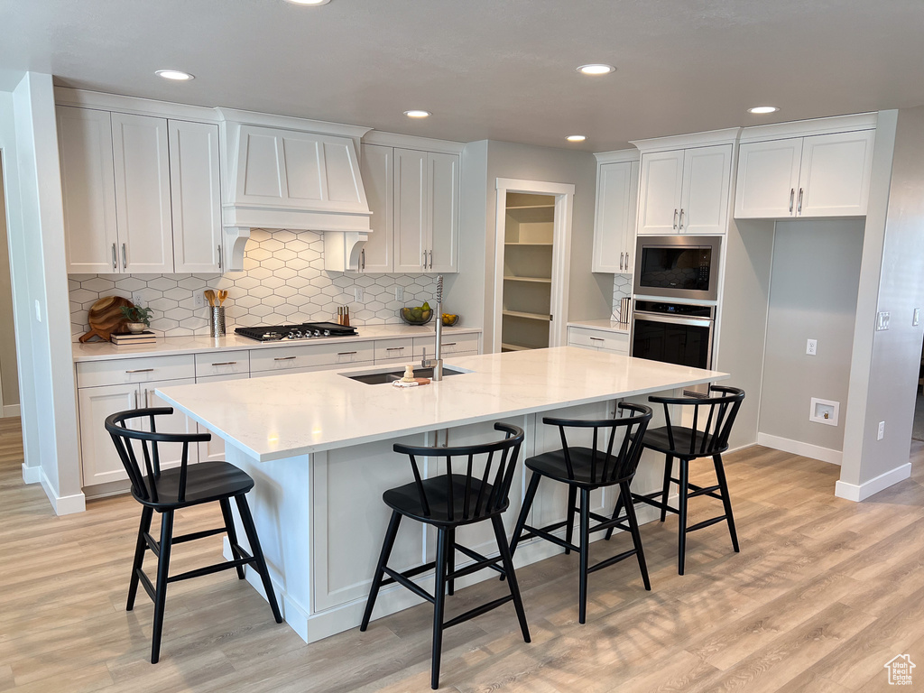 Kitchen with light hardwood / wood-style flooring, white cabinetry, sink, an island with sink, and a kitchen breakfast bar