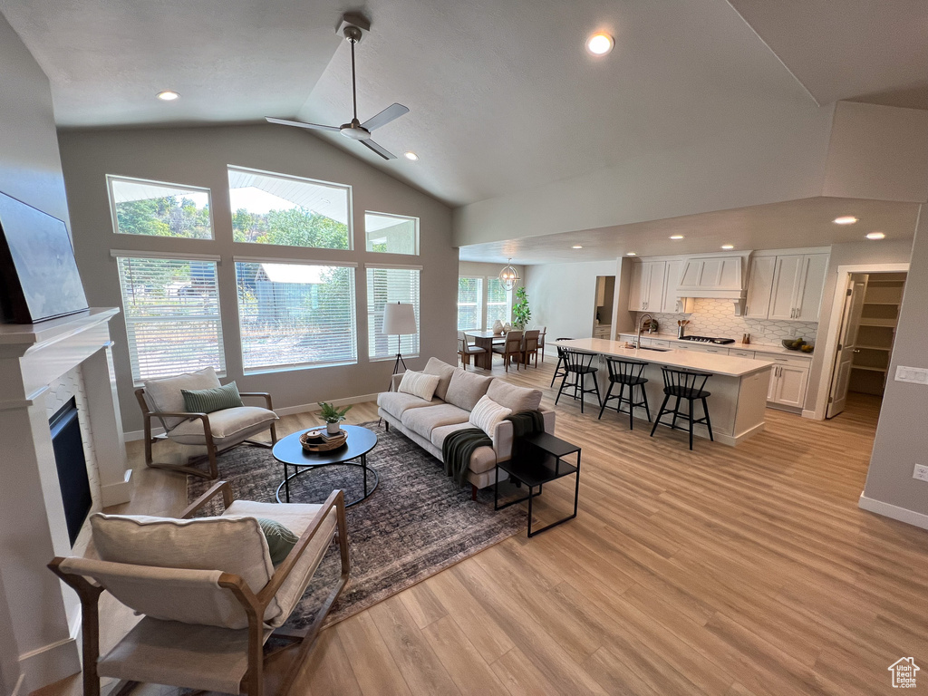 Living room featuring a high end fireplace, light hardwood / wood-style floors, sink, high vaulted ceiling, and ceiling fan