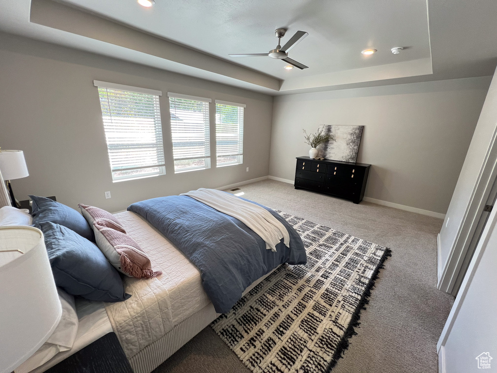 Carpeted bedroom featuring a tray ceiling and ceiling fan