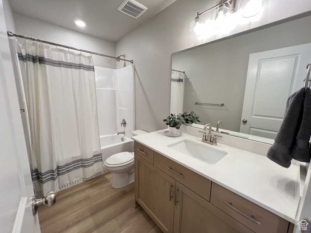 Full bathroom with vanity, toilet, shower / bath combination with curtain, and hardwood / wood-style floors