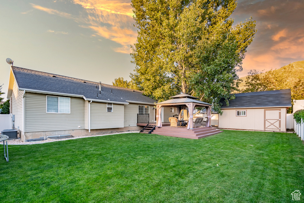 Back house at dusk with a yard, central AC, a shed, and a wooden deck