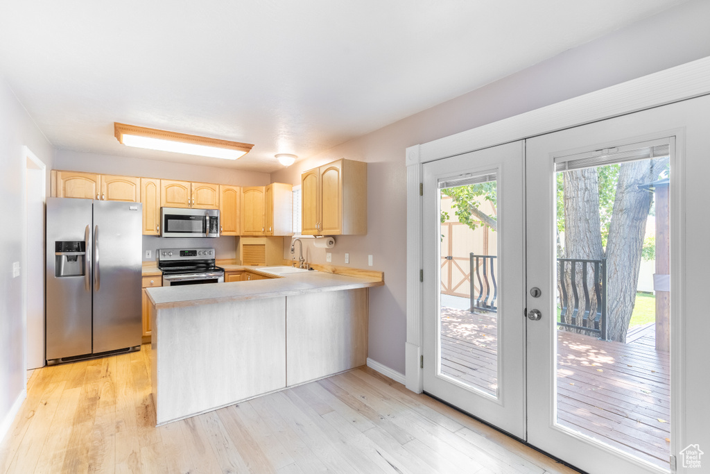 Kitchen featuring kitchen peninsula, light hardwood / wood-style floors, appliances with stainless steel finishes, light brown cabinetry, and sink