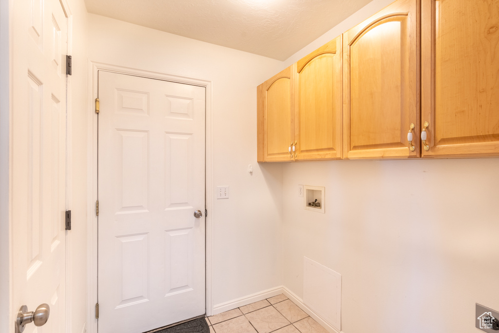 Laundry area with hookup for a washing machine, light tile patterned floors, and cabinets