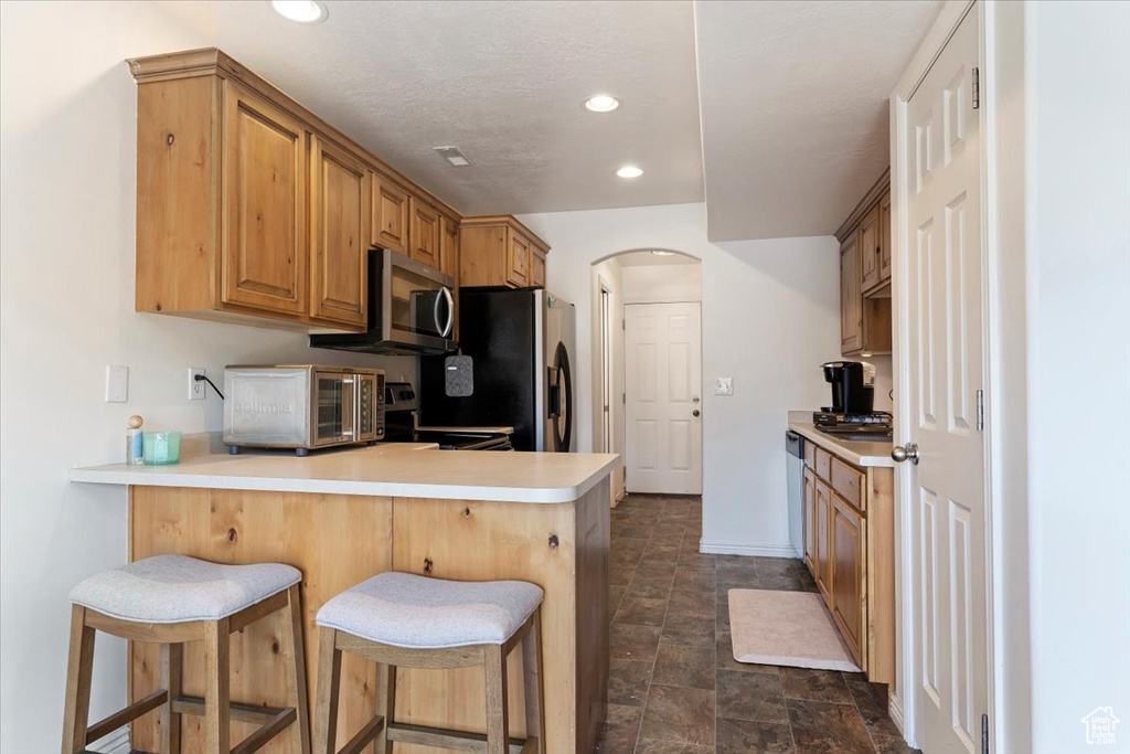 Kitchen with a kitchen bar, appliances with stainless steel finishes, kitchen peninsula, and dark tile patterned flooring