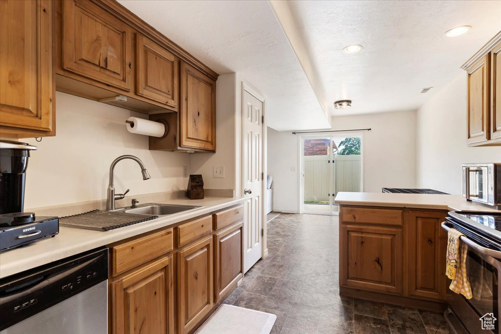 Kitchen with stove, dark tile patterned floors, sink, kitchen peninsula, and stainless steel dishwasher