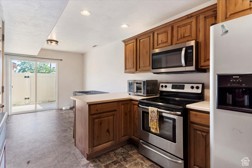 Kitchen with appliances with stainless steel finishes, kitchen peninsula, and dark tile patterned floors