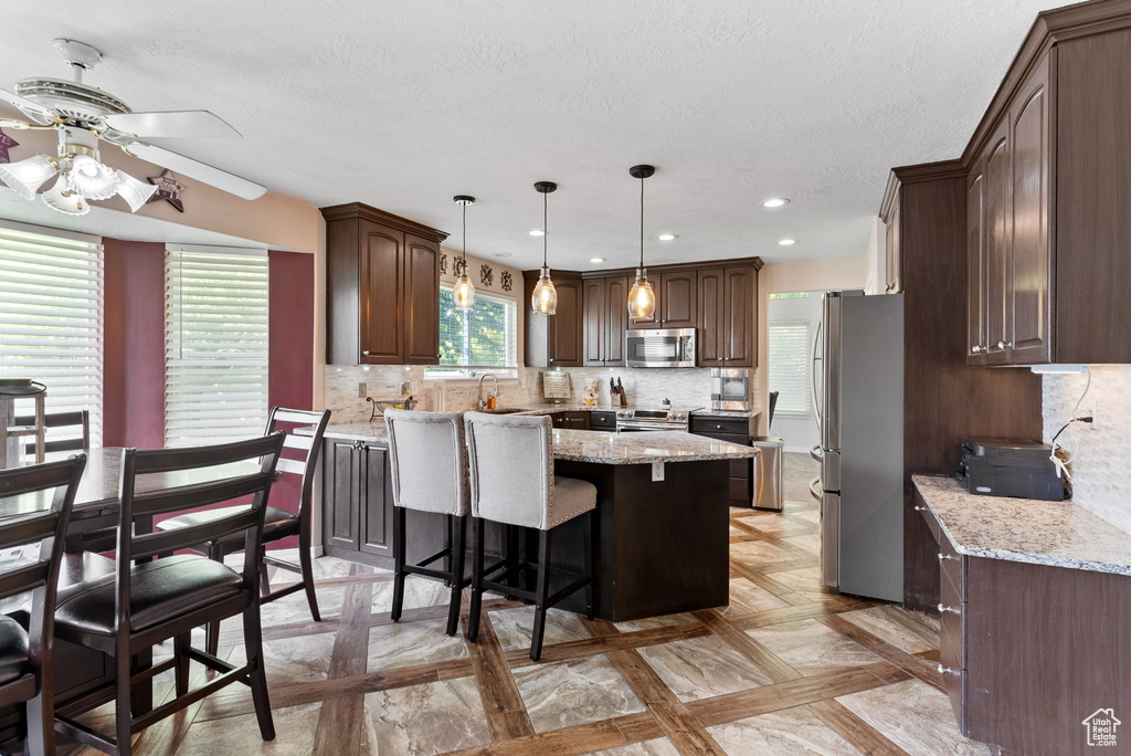 Kitchen with light stone counters, ceiling fan, stainless steel appliances, decorative backsplash, and decorative light fixtures