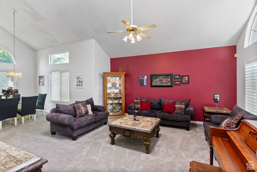 Carpeted living room with high vaulted ceiling and ceiling fan with notable chandelier