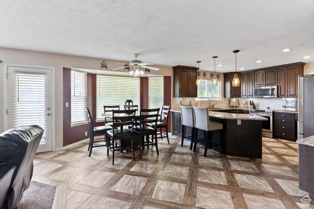 Kitchen featuring stainless steel appliances, light stone countertops, dark brown cabinetry, and backsplash