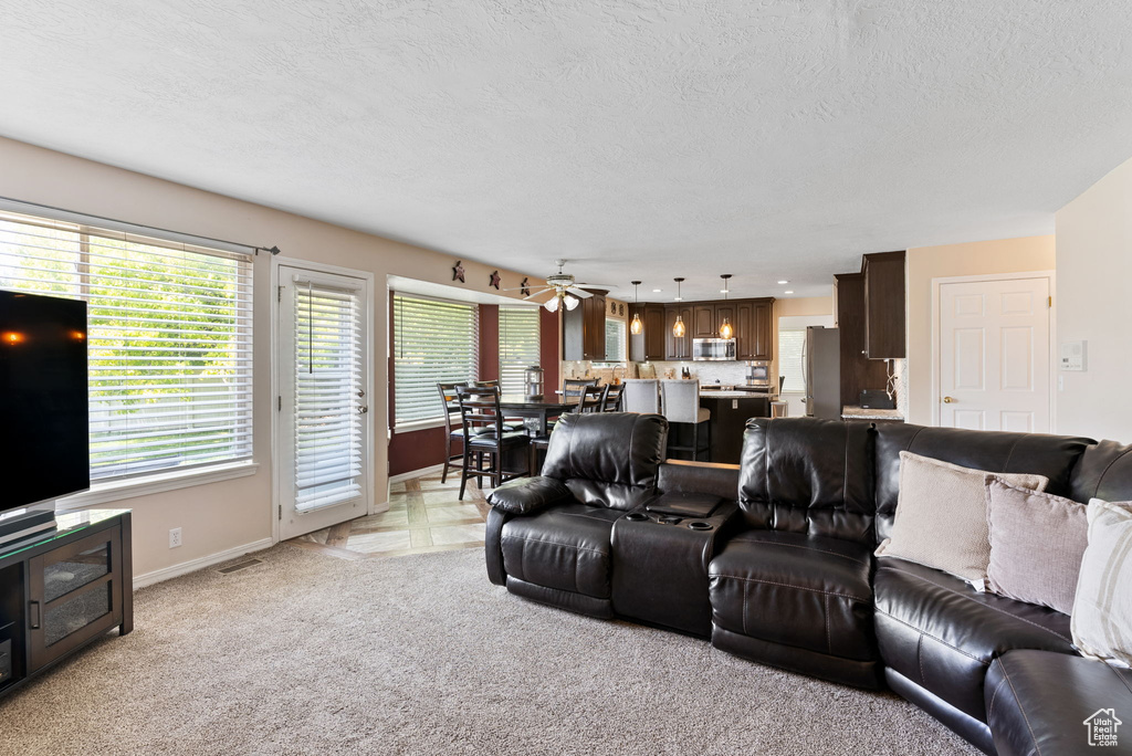 Living room with a textured ceiling, light colored carpet, and ceiling fan