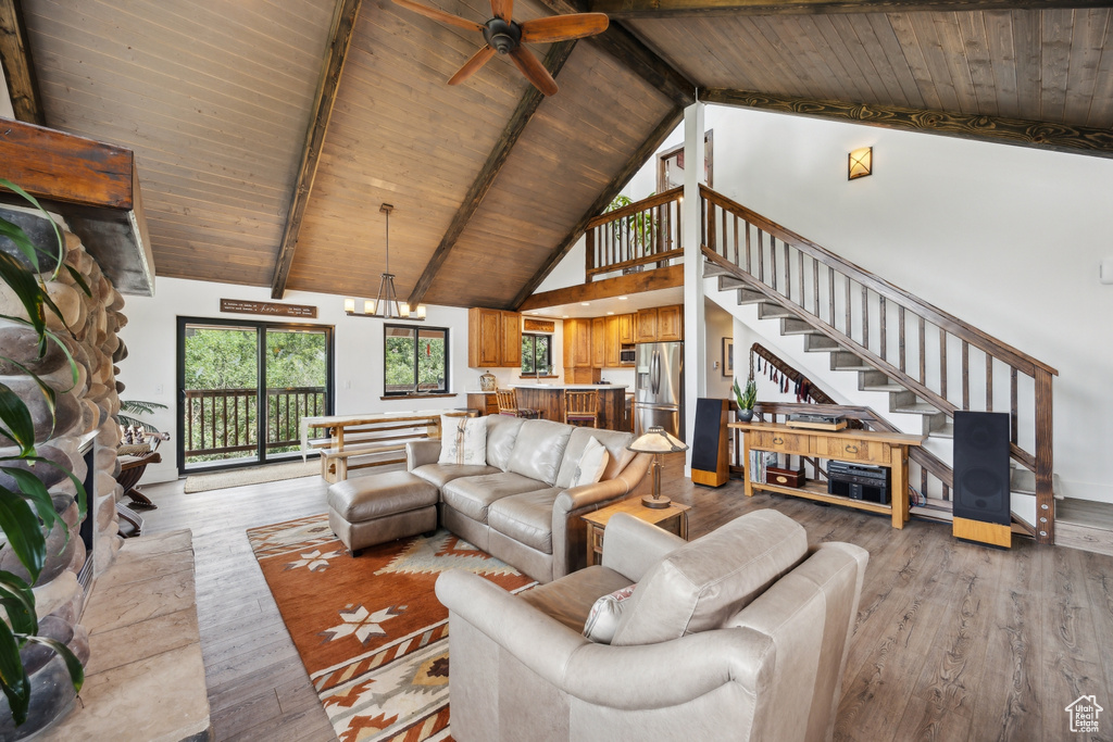 Living room featuring light wood-type flooring, ceiling fan with notable chandelier, beamed ceiling, wooden ceiling, and high vaulted ceiling