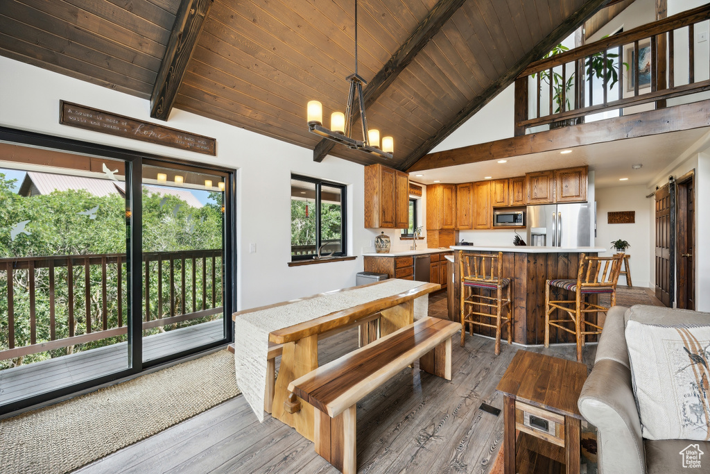 Dining space with high vaulted ceiling, an inviting chandelier, beam ceiling, light hardwood / wood-style floors, and wood ceiling