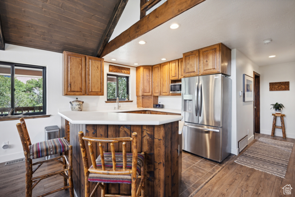 Kitchen with lofted ceiling, a breakfast bar area, kitchen peninsula, appliances with stainless steel finishes, and hardwood / wood-style flooring