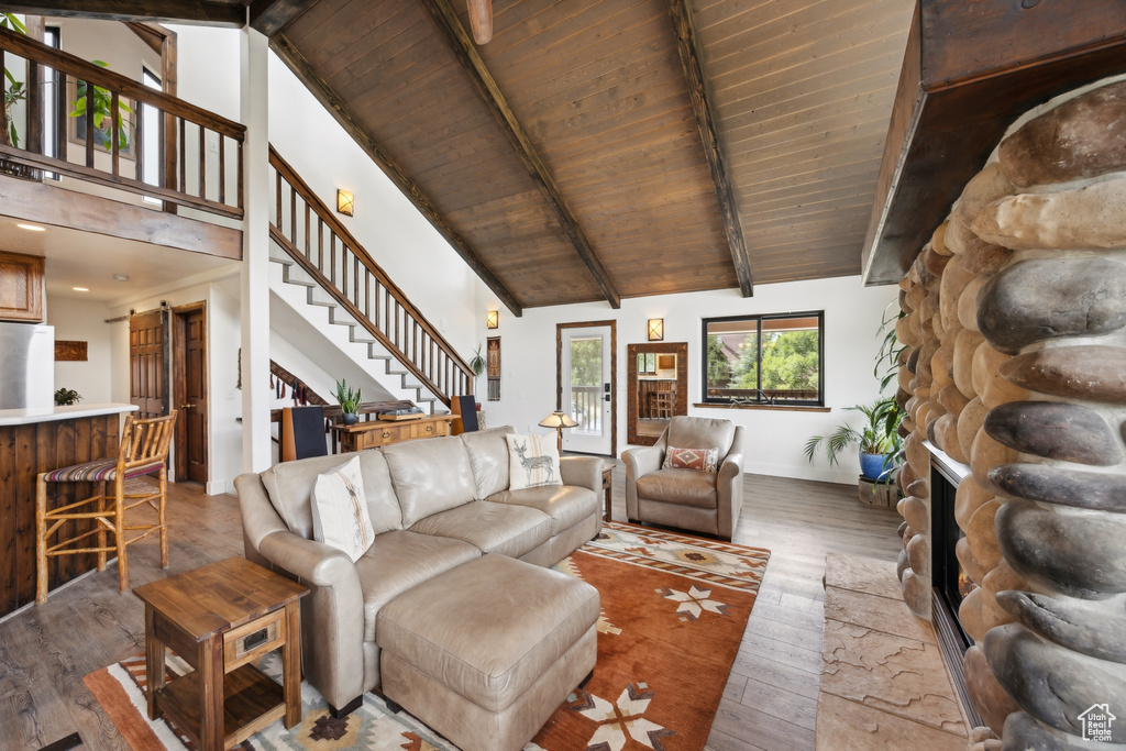 Living room with high vaulted ceiling, hardwood / wood-style floors, beam ceiling, a stone fireplace, and wood ceiling