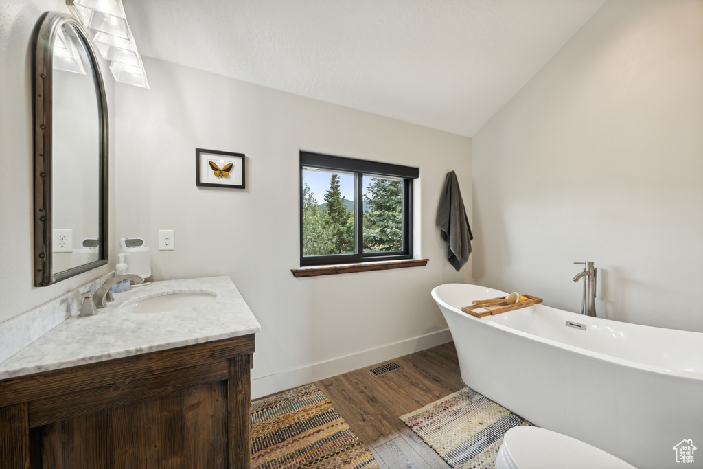 Bathroom featuring lofted ceiling, toilet, vanity, a bathing tub, and hardwood / wood-style flooring