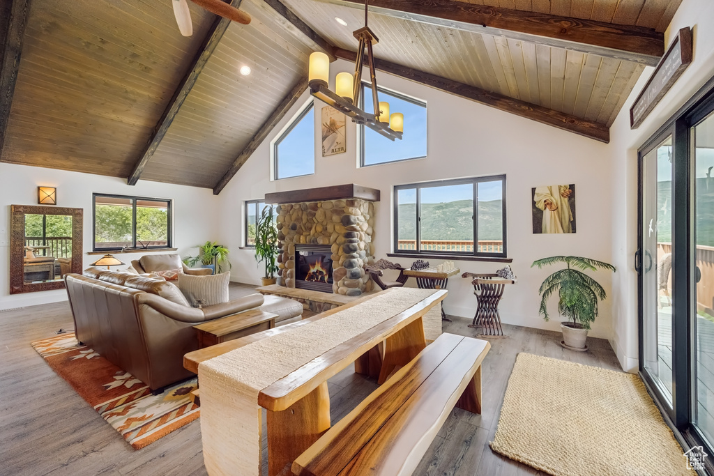 Living room featuring beamed ceiling, wood ceiling, a stone fireplace, light wood-type flooring, and high vaulted ceiling