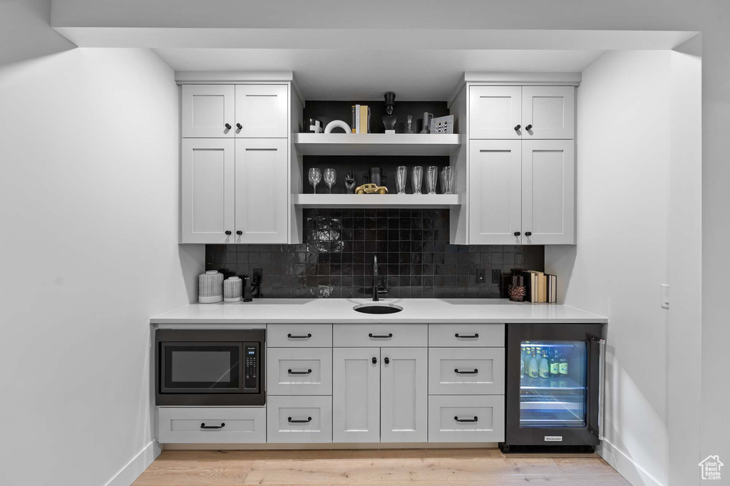 Bar with white cabinets, black microwave, wine cooler, and light hardwood / wood-style flooring