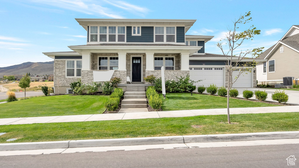 View of front facade with a mountain view, a garage, a front yard, central air condition unit, and covered porch