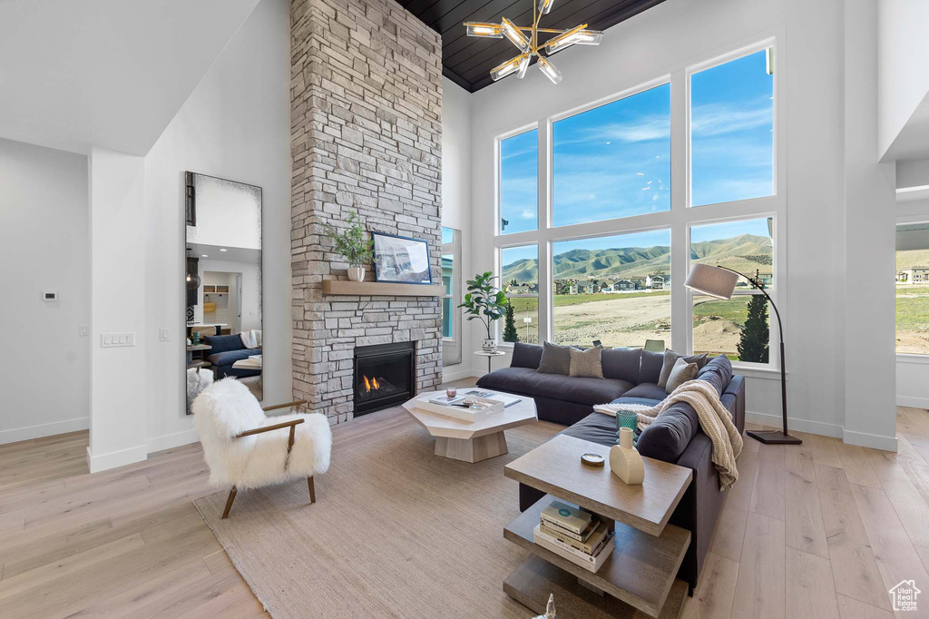 Living room with high vaulted ceiling, a stone fireplace, a chandelier, and light wood-type flooring