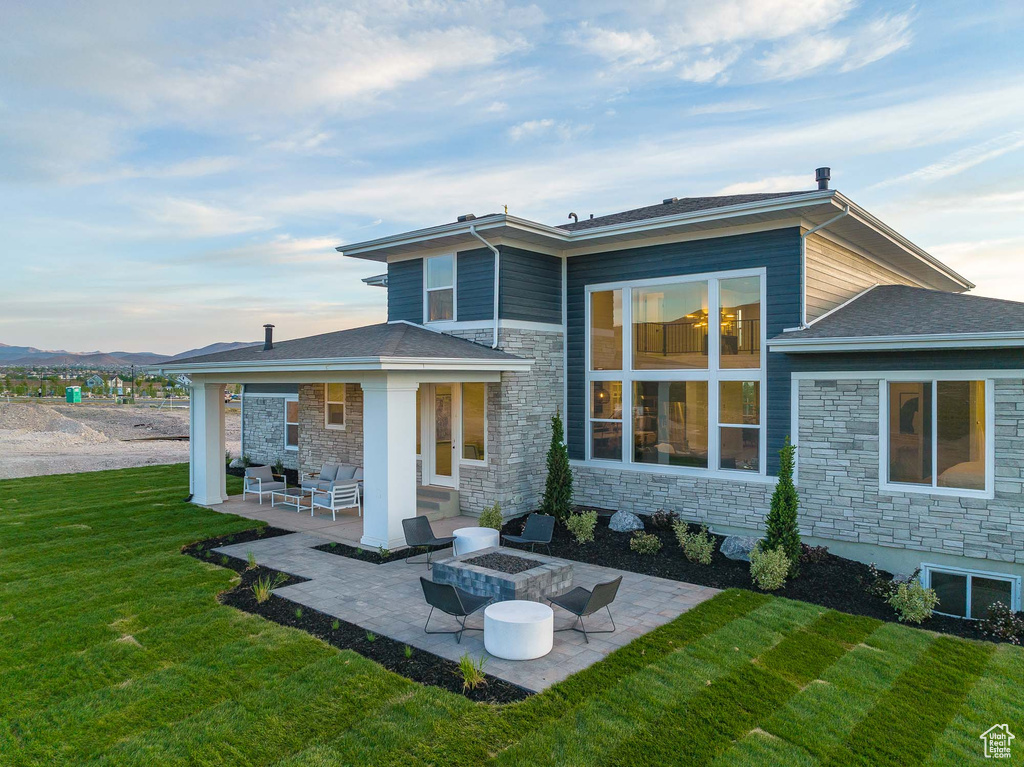 Back house at dusk with a patio, a lawn, and a fire pit