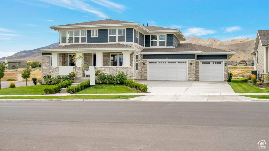 View of front of house featuring a mountain view, a front lawn, a porch, central AC unit, and a garage