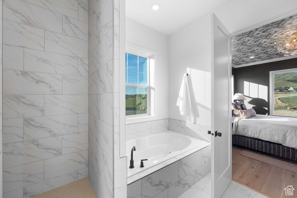 Bathroom with a relaxing tiled bath and wood-type flooring