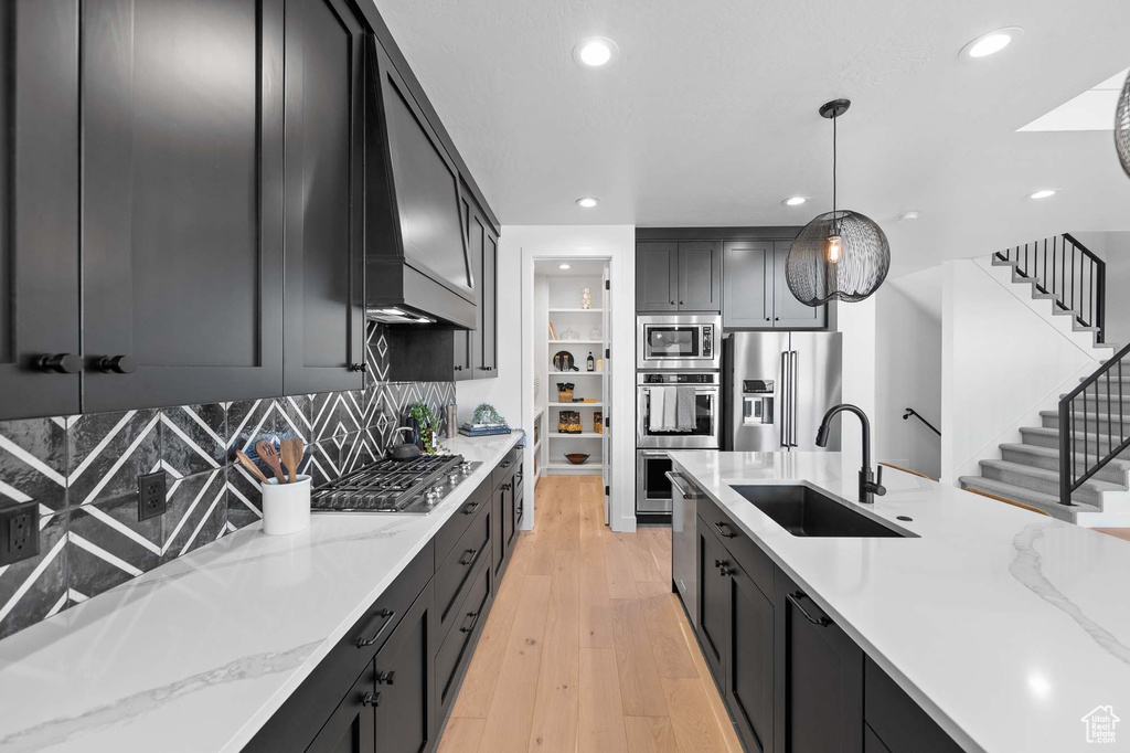 Kitchen featuring light stone counters, light hardwood / wood-style flooring, tasteful backsplash, appliances with stainless steel finishes, and sink