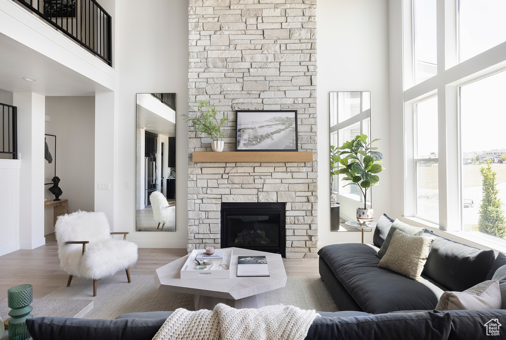 Living room with a high ceiling, a stone fireplace, a wealth of natural light, and wood-type flooring