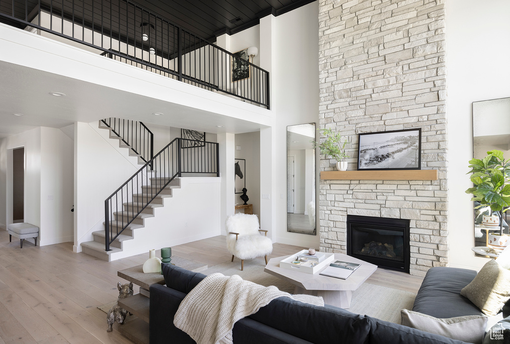 Living room with a stone fireplace, a towering ceiling, and light hardwood / wood-style flooring